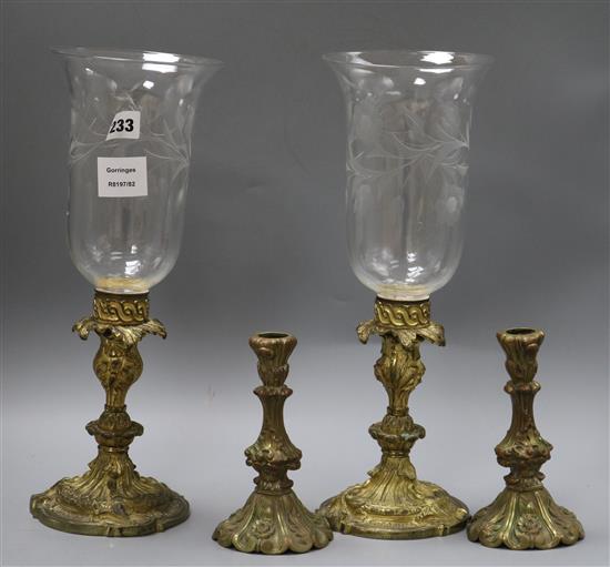 A pair of Victorian gilt metal candlesticks, cast and chased with foliage, with etched campana form storm shades